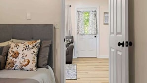 A bedroom with a bed, a bedside table, a chair, and a door leading to another room. - Peaceful Woodland Cottage Near Hendersonville (Hendersonville)