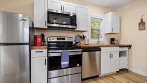 A modern kitchen with stainless steel appliances, white cabinetry, and a wooden countertop. - Peaceful Woodland Cottage Near Hendersonville (Hendersonville)
