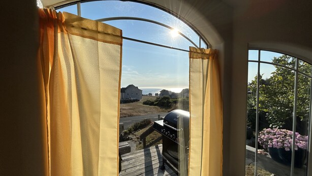 A room with a large arched window, a barbecue grill outside, and a view of a house and landscape.