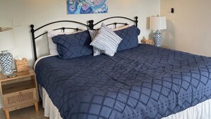 A neatly made bed with a dark blue quilt and white skirted bed skirt, flanked by two bedside tables with lamps and decorative vases.