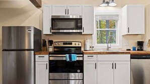 A modern kitchen with stainless steel appliances, white cabinets, and a window providing natural light. - Cozy Woodland 1BR Cottage Near Trails (Hendersonville)