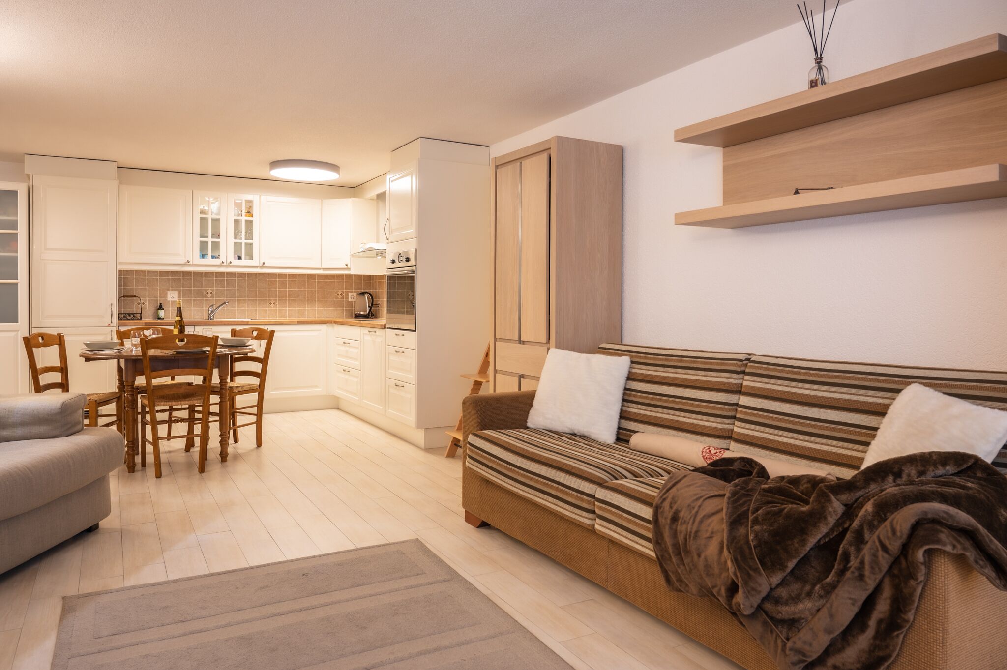 A modern living room with a sofa, a dining table with chairs, and a kitchen area with cabinets and appliances.