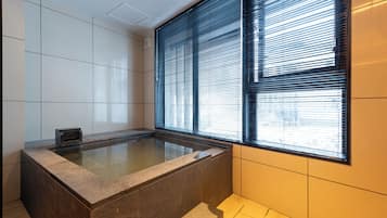 A modern bathroom with a freestanding bathtub, large windows with blinds, and tiled walls.