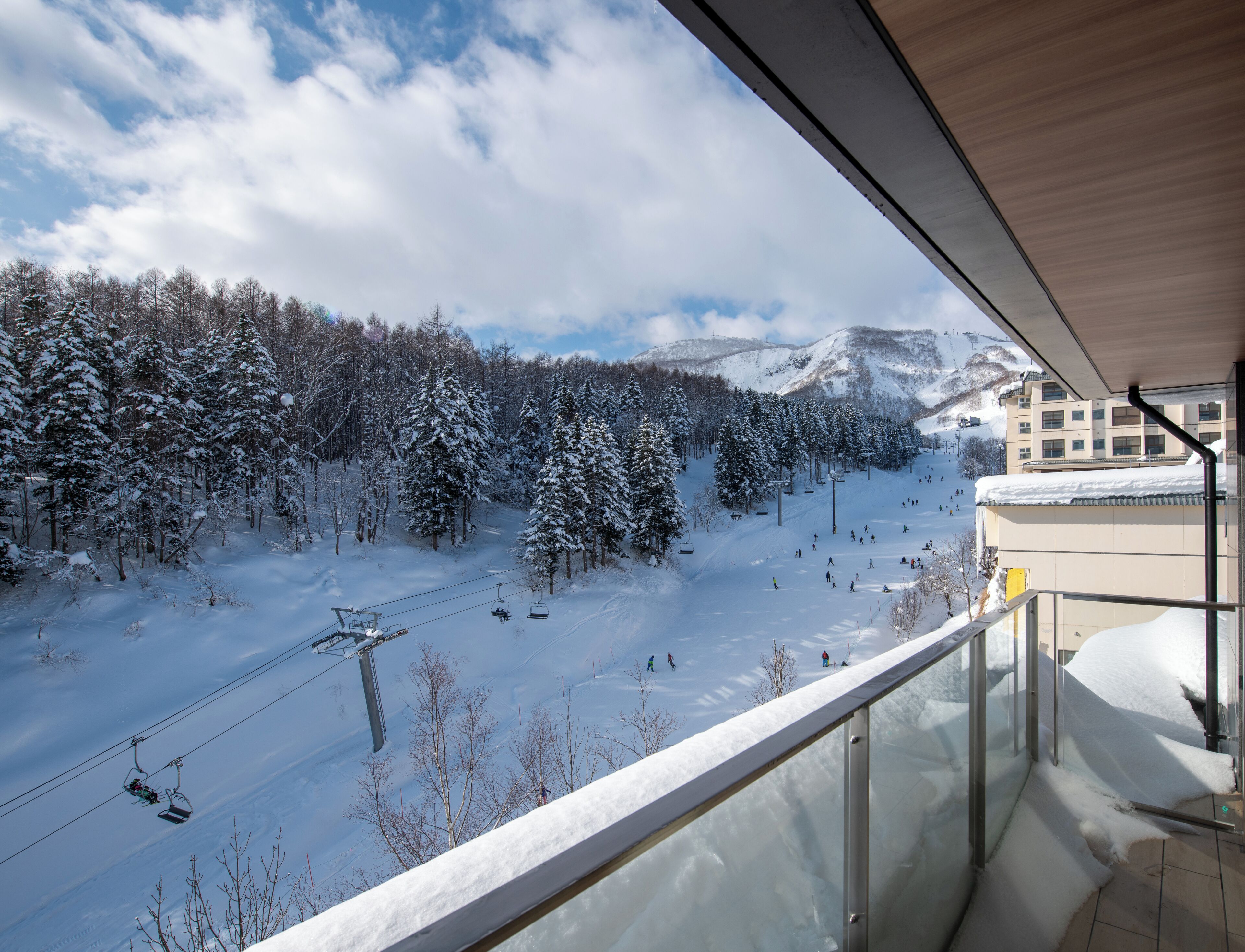A snowy mountain landscape with a ski lift and a building with a balcony overlooking the scene.