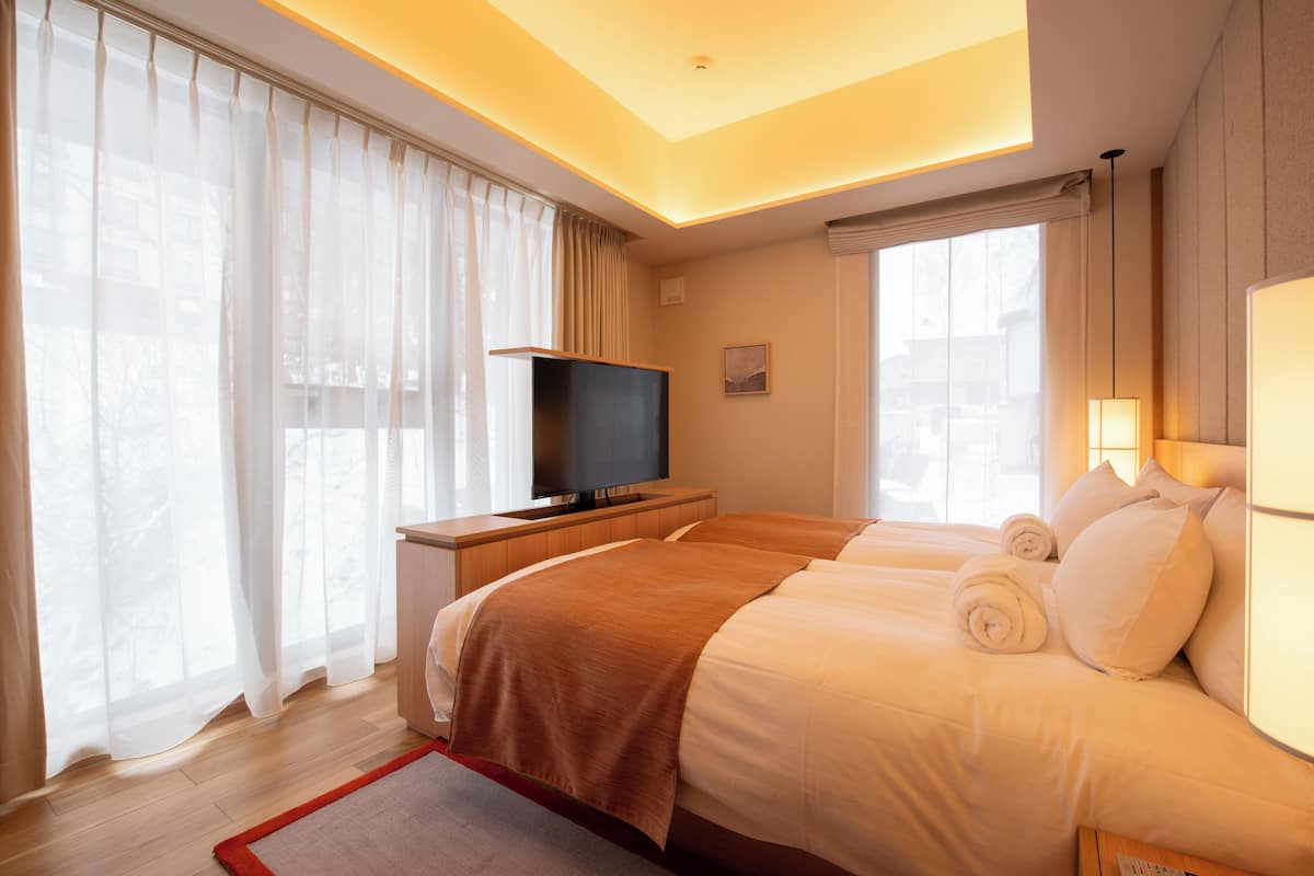 A hotel room with a bed, a TV, a desk, and a window with curtains.