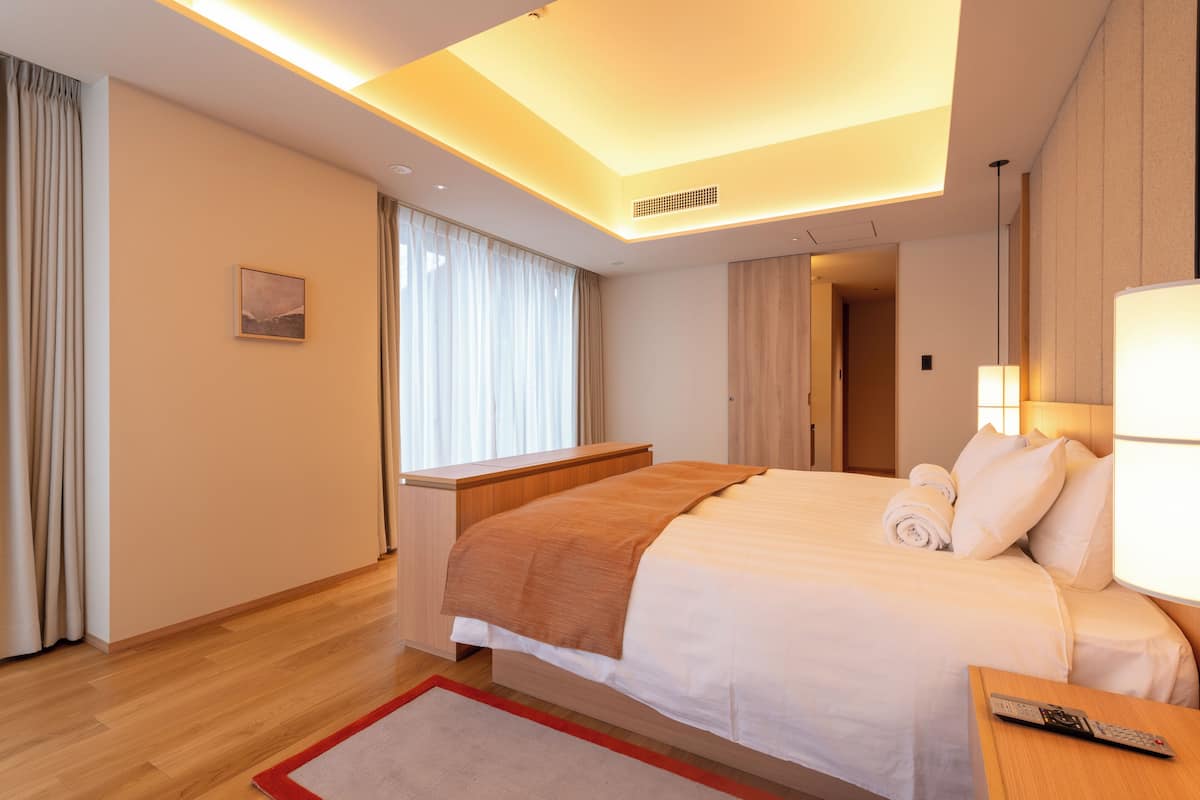 A modern hotel room with a large bed, bedside lamps, a wooden nightstand, and a view of the hallway.