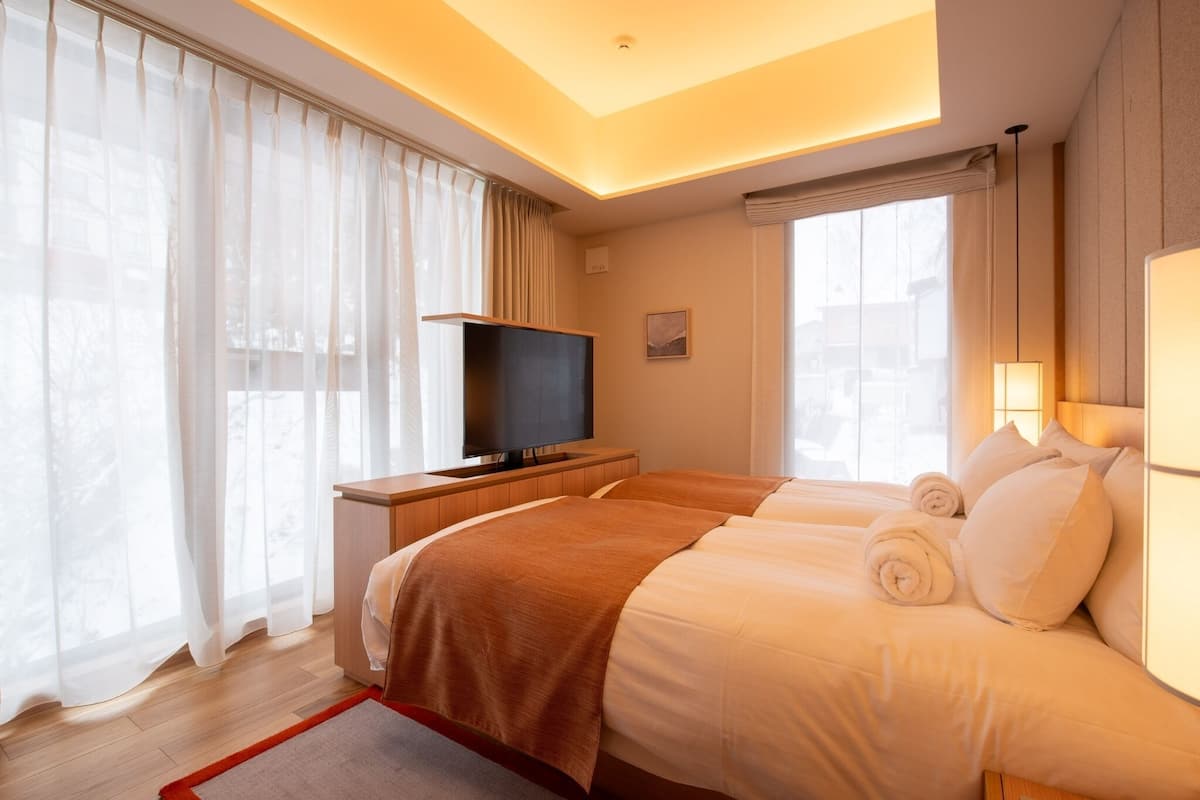 A hotel room with a bed, a television, and a window with curtains.