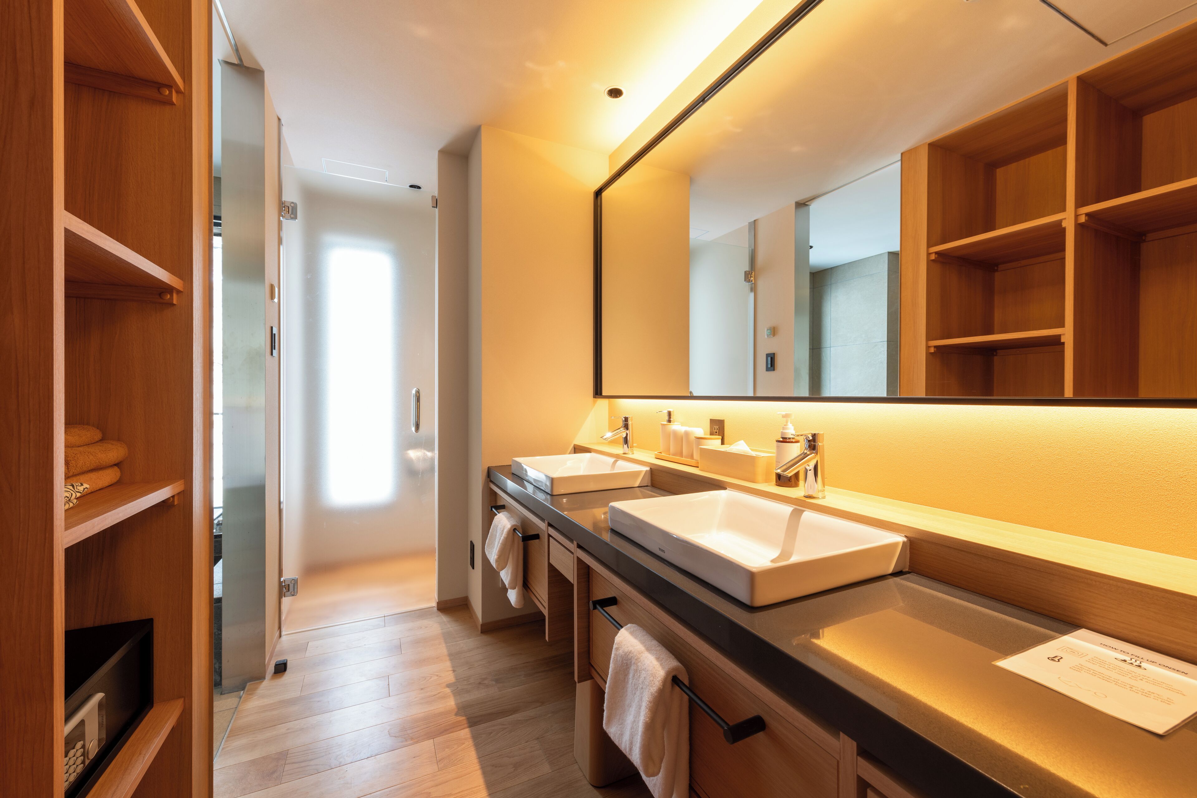 Un baño moderno con dos lavamanos, un espejo grande y estantes de madera.