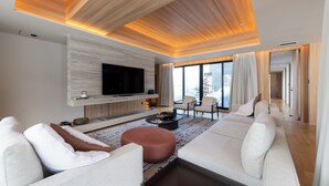 Un salon moderne doté d’un téléviseur à écran plat, de sièges confortables et d’une grande fenêtre offrant une vue sur la ville.