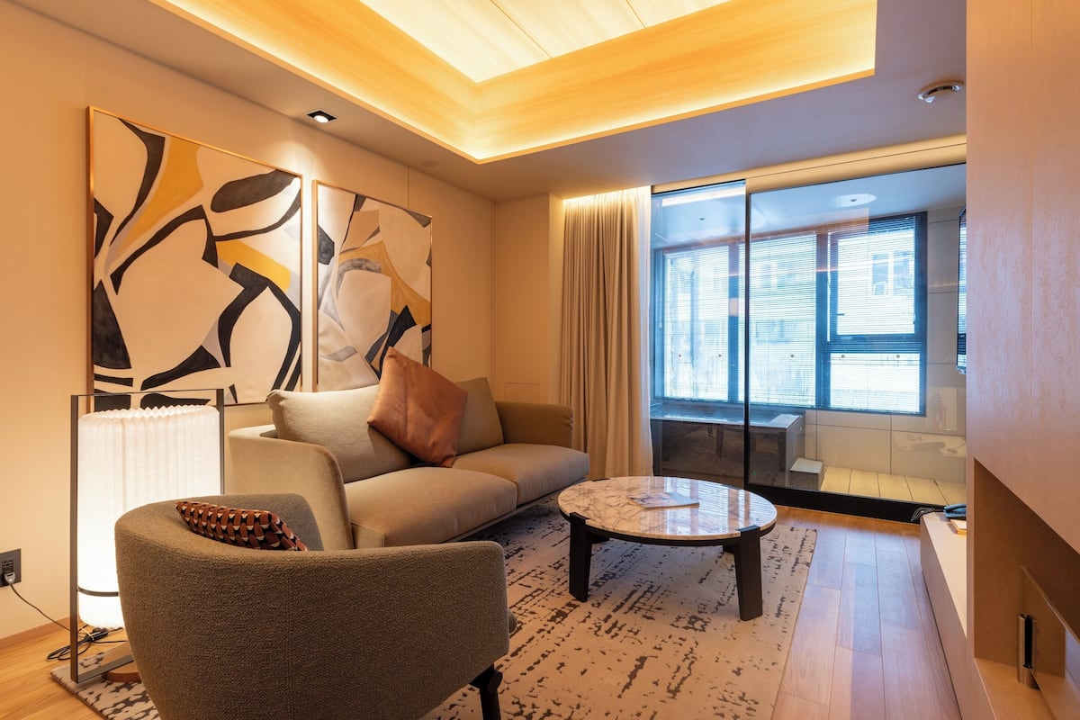 A modern living room with a sofa, armchair, coffee table, abstract art, and large windows.