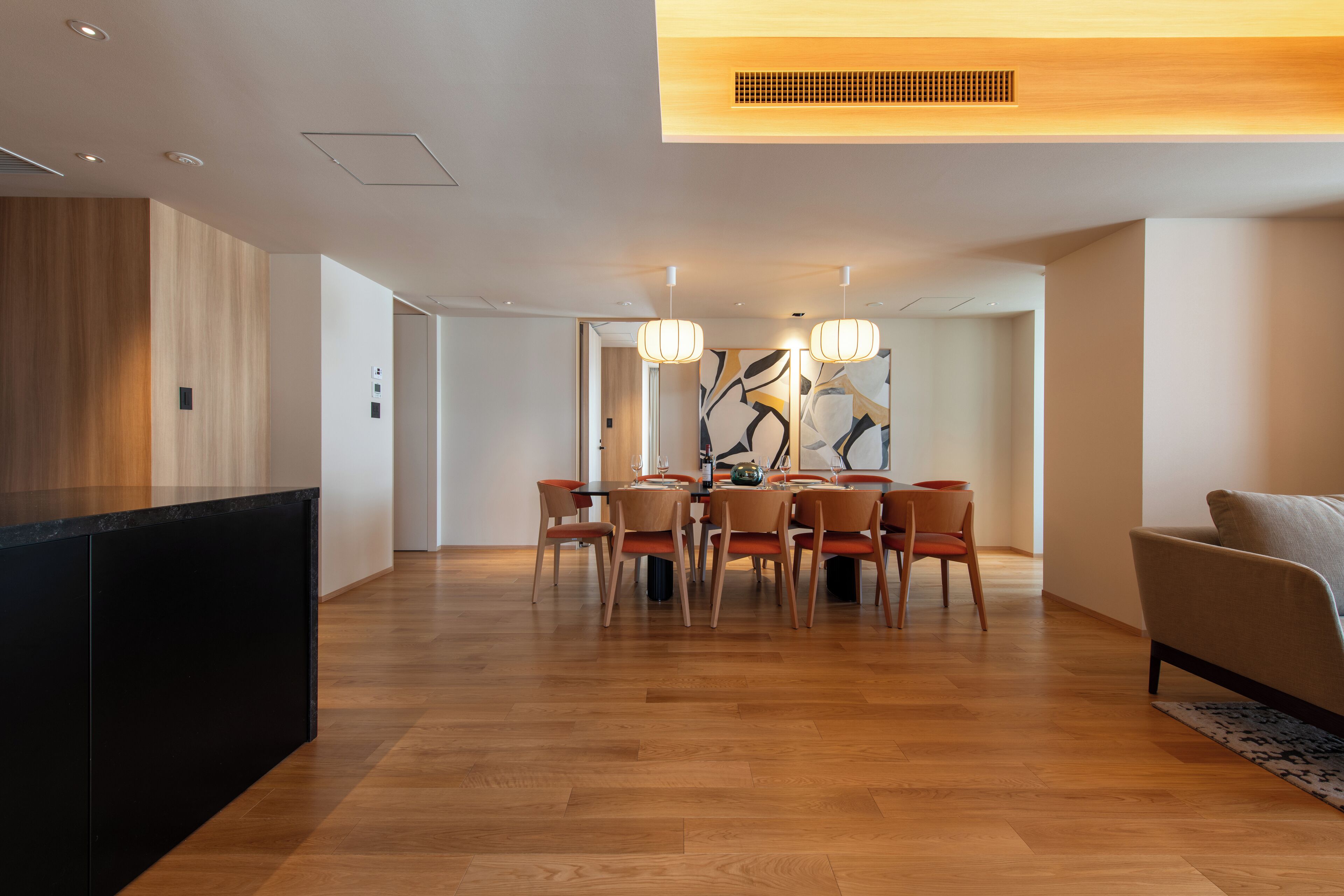 A modern dining area with a wooden floor, a black island, and a dining table with chairs. There is a sofa and a rug in the foreground.