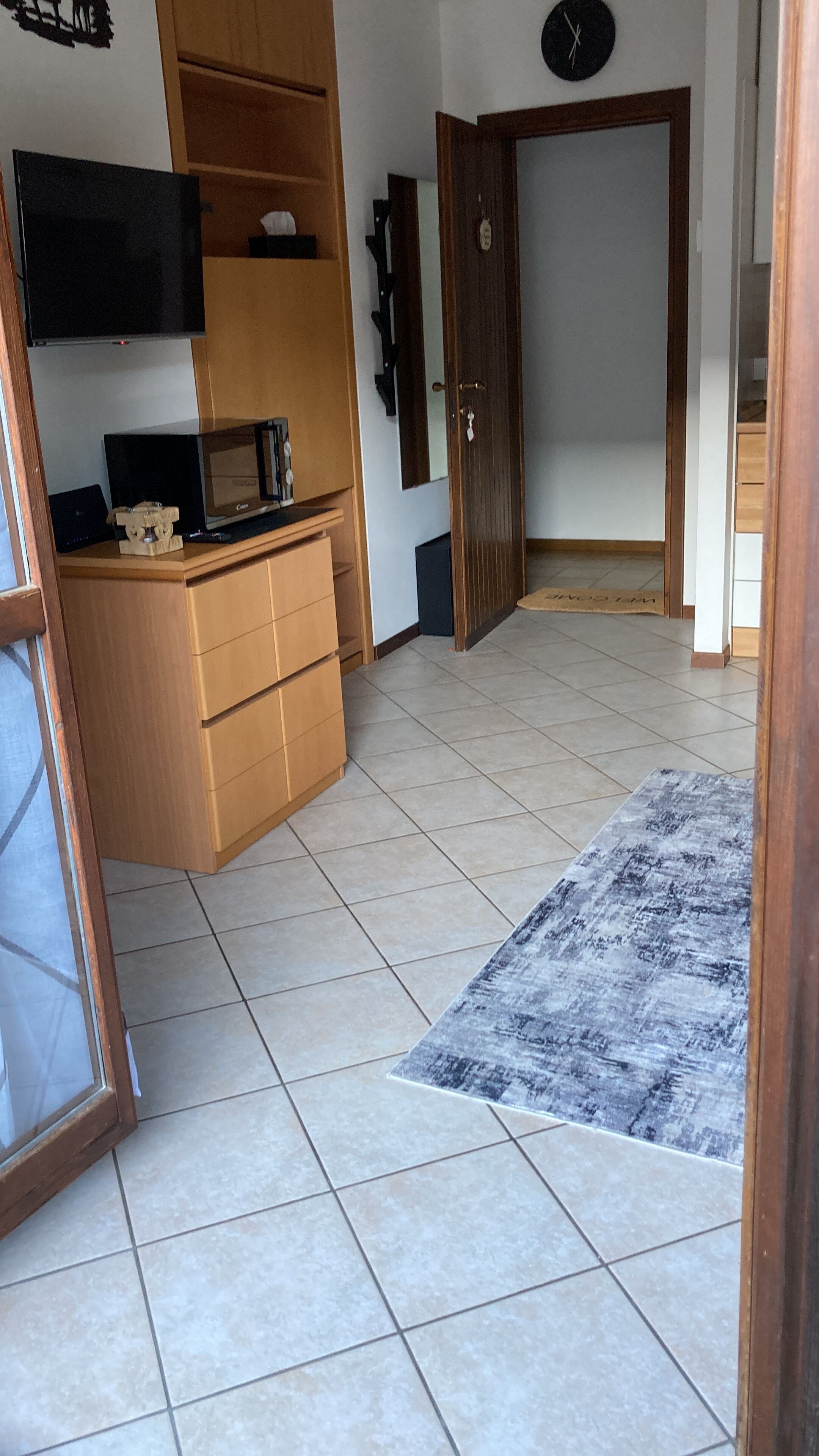 Een kamer met een betegelde vloer, een houten kast, een magnetron, een flatscreen televisie en een deur met sleutelslot.