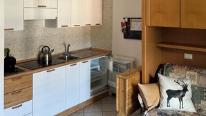 A modern kitchen with white cabinets, a wooden countertop, and a built-in oven. There is a sofa with patterned cushions and a decorative pillow with a deer design. - Cozy Giava's Mountain Place in downtown Aprica (Aprica)