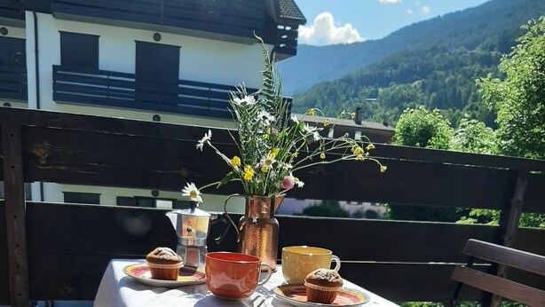 A table set outdoors with a view of mountains, a wooden fence, and a building in the background. - Cozy Giava's Mountain Place in downtown Aprica (Aprica)