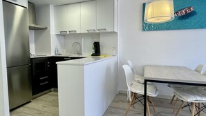 A modern kitchen with white cabinets, a stainless steel refrigerator, and a dining area with a table and chairs. - FESTASTAR 212 (Estartit)