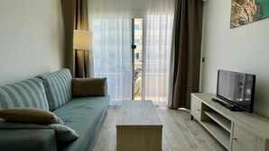 A living room with a sofa, a coffee table, a TV on a stand, and a view through a glass door. - FESTASTAR 212 (Estartit)