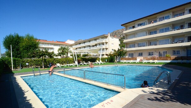 A swimming pool with a wooden deck, surrounded by lounge chairs and a building with multiple balconies. - FESTASTAR 212 (Estartit)