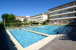 A swimming pool with a wooden deck, surrounded by lounge chairs and a building with multiple balconies. - FESTASTAR 212 (Estartit)