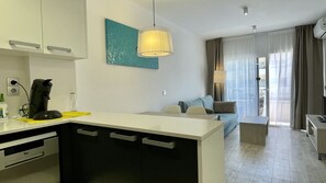A modern kitchen with a central island, a dining area with a sofa, and a view of the outdoors through large windows.