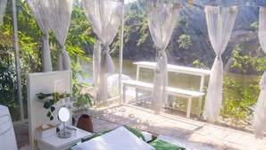 A bedroom with a bed, bedside table, and a view of a lake. - The Three Bubble Houses (Sai Yok)