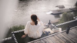 A person sitting on a dock overlooking a body of water, with a book and a bottle nearby. - The Three Bubble Houses (Sai Yok)