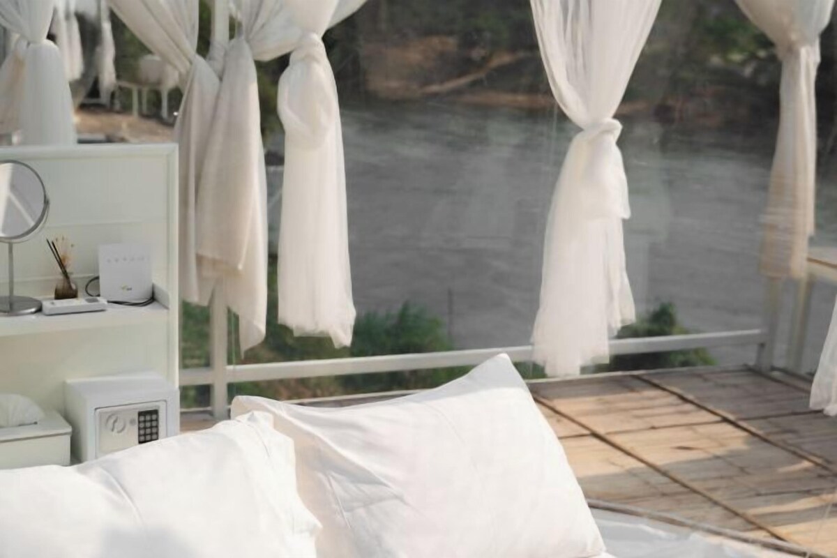 A room with a bed, a bedside table with a lamp, a mirror, and a window with curtains.