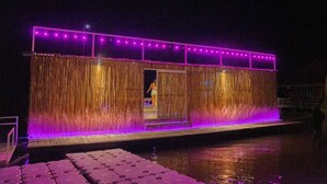 A waterfront building with a covered entrance, illuminated by purple lights, and a dock extending into the water. - The Three Bubble Houses (Sai Yok)