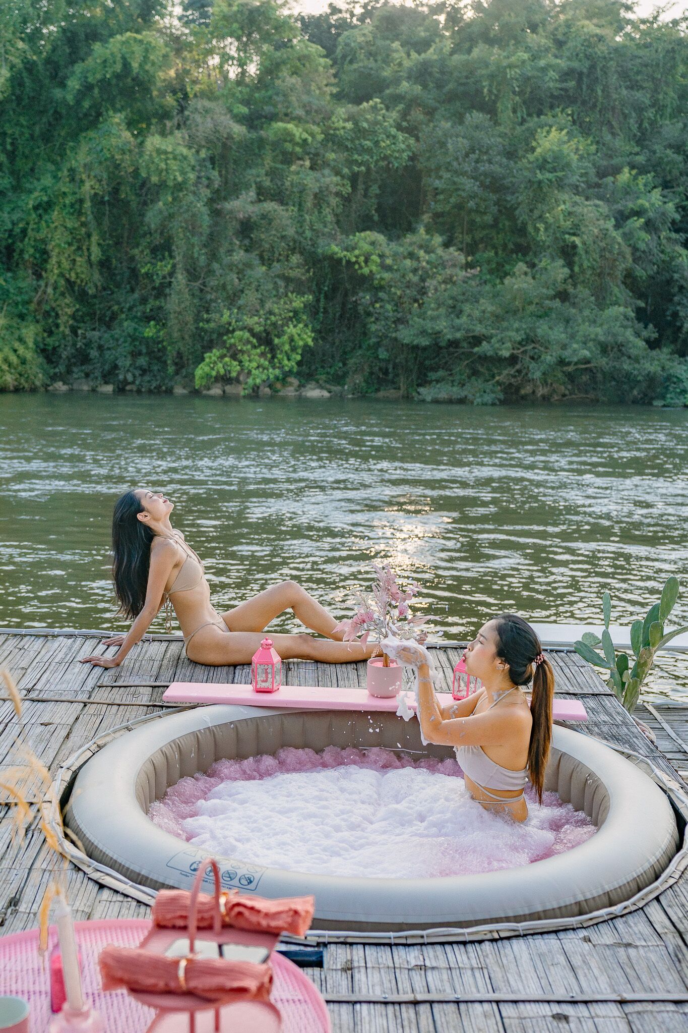 A wooden deck with a hot tub surrounded by greenery and a river.