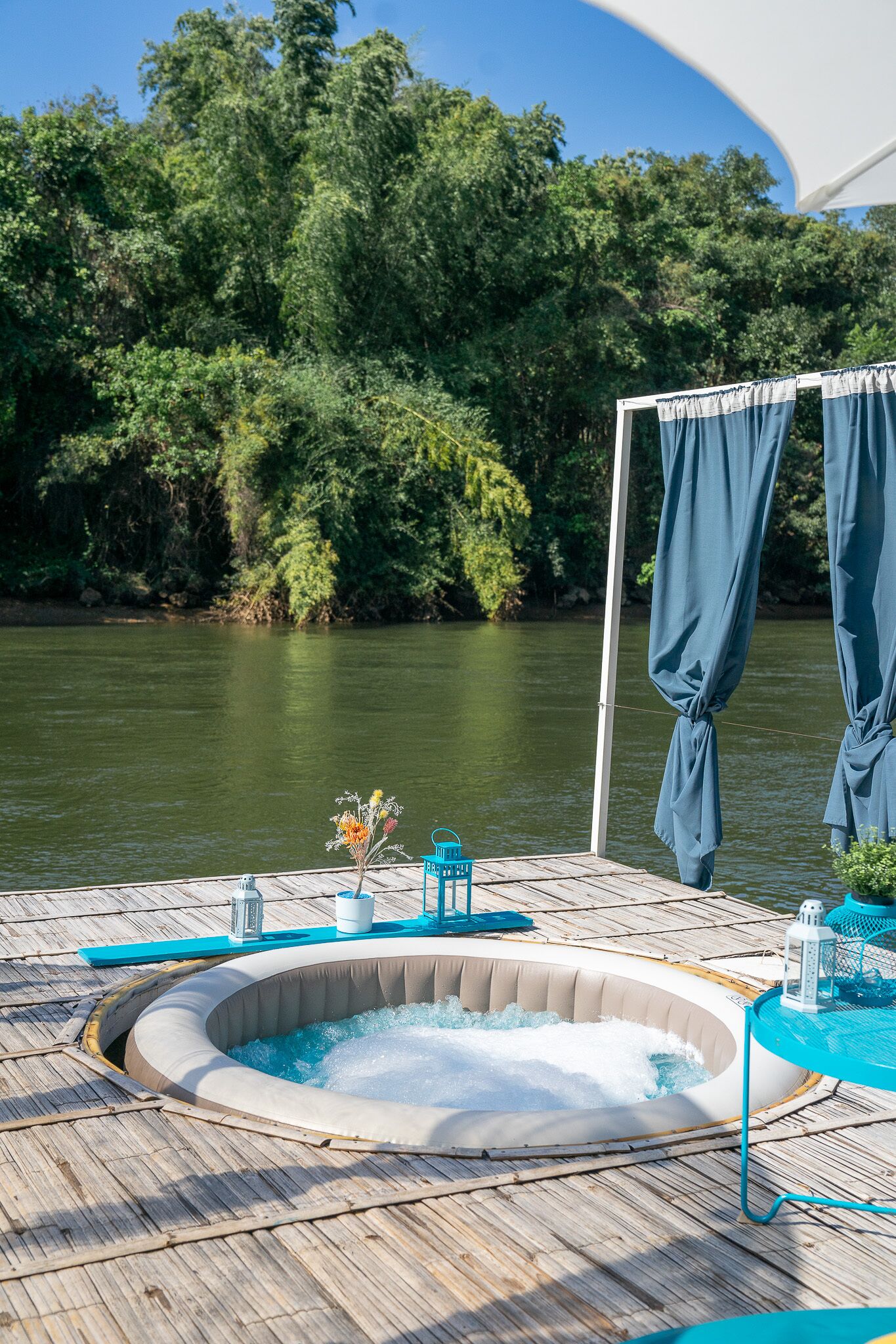 A hot tub on a wooden deck with a river view, surrounded by greenery.