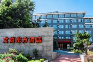 A hotel entrance with a sign in Chinese characters, a pathway leading to the entrance, and a building with multiple floors and windows.