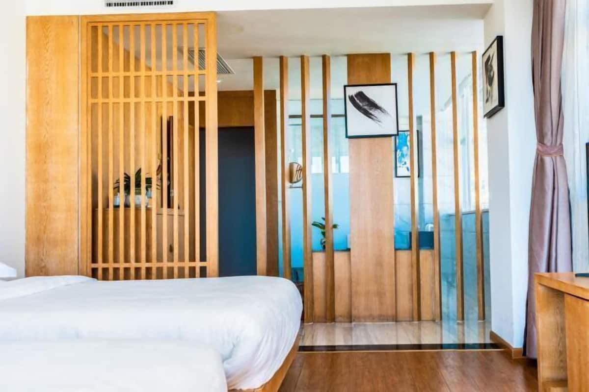 A hotel room with a bed, a wooden partition, and a view of the outside.