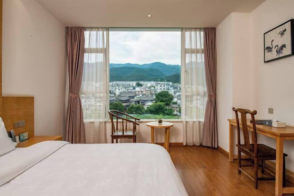 A hotel room with a bed, a desk, a chair, a small table, and a window with curtains.