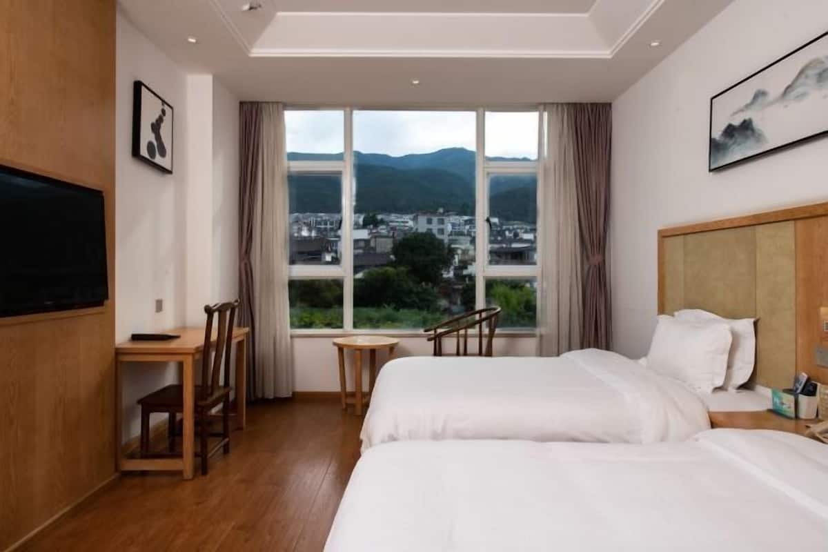 A hotel room with two beds, a desk, a chair, a TV, and a large window with a city view.