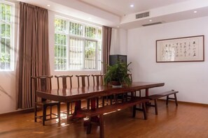 A conference room with a long wooden table, chairs, a bench, a potted plant, and a framed artwork on the wall. - Dali Wenyue Hotel (Erhai Ecological Corridor Branch) (Dali City)