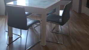 A dining area with a glass-top table, four chairs, and a hanging light fixture. - Charmant Appartement de Village (Roquebrune-sur-Argens)