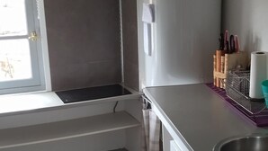 A modern kitchen with white cabinets, a stainless steel sink, and a built-in oven. There are hanging utensils above the sink and a window with a view of the outside. - Charmant Appartement de Village (Roquebrune-sur-Argens)