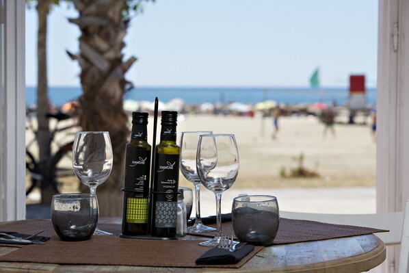 A table with wine bottles and glasses, a napkin, and cutlery, with a view of the beach and ocean through a window. - Apartamento Paris (Miami Playa)
