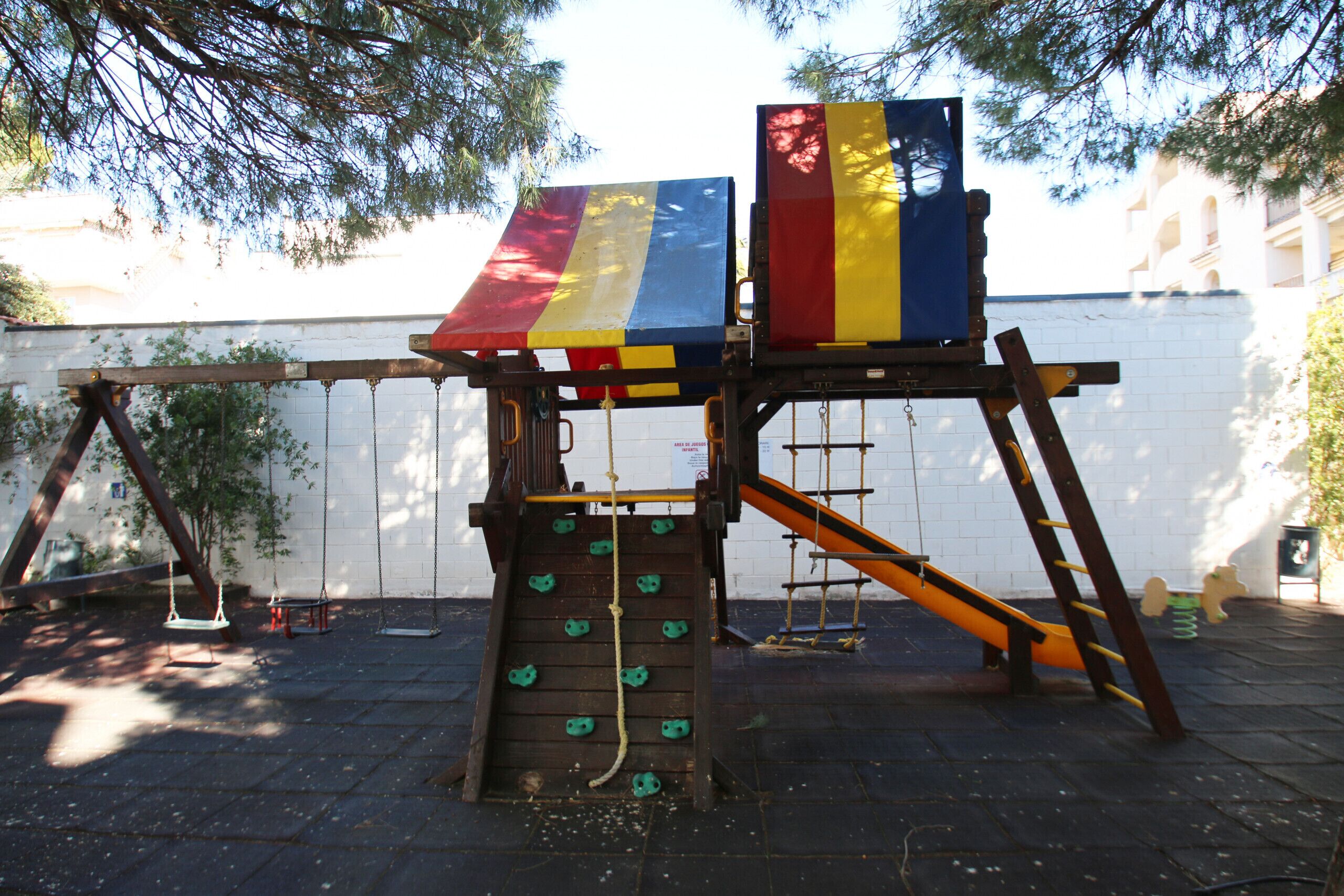 A playground with a wooden climbing wall, swings, and a slide.