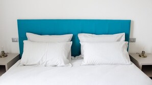 Un lit avec une literie blanche et une tête de lit de couleur turquoise dans une chambre d’hôtel.