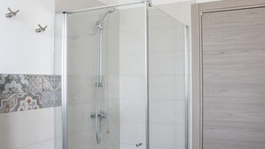 Une douche fermée par des parois de verre, avec un cadre en chrome, des murs recouverts de carreaux blancs et une porte en bois.
