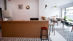Un espace d’accueil moderne avec un comptoir en bois, un fauteuil de bureau noir et un coin repas avec des tables et des chaises.