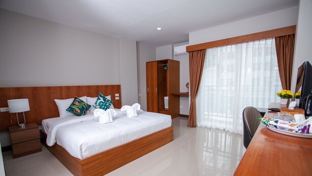 Une chambre d’hôtel avec un lit en bois, un bureau avec une chaise, une armoire et une grande fenêtre avec des rideaux.