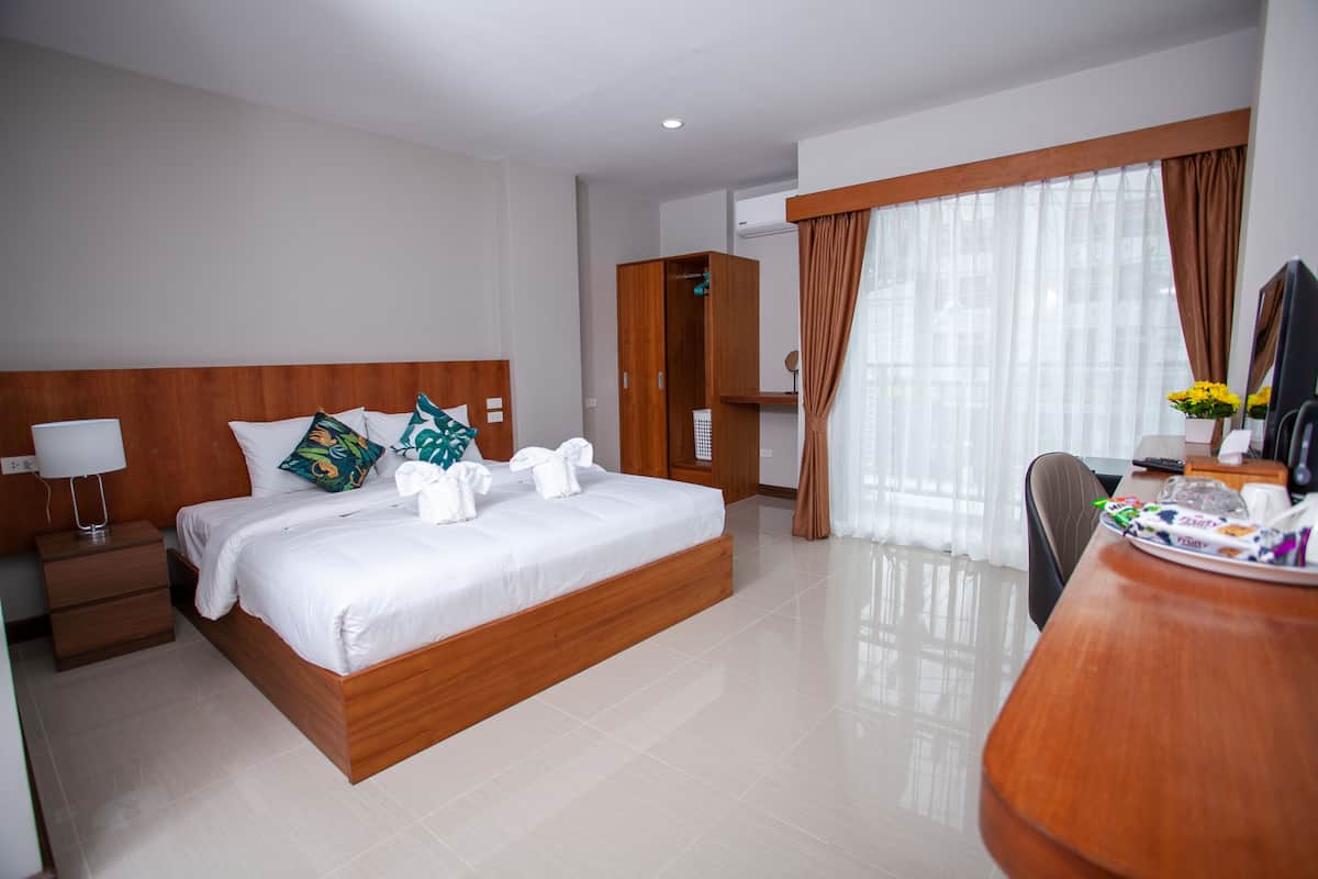 Ein Hotelzimmer mit einem hölzernen Bett, einem Schreibtisch mit Stuhl, einem Kleiderschrank und einem großen Fenster mit Vorhängen.