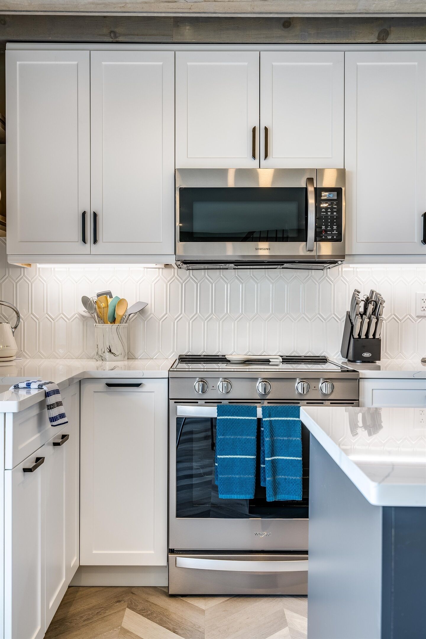 A modern kitchen with white cabinetry, a stainless steel microwave, a gas stove, and an oven.
