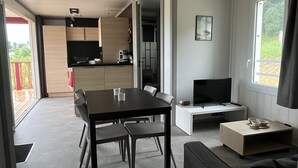 A modern living room with a dining area, a TV, and a kitchen visible through an open door. - Chalet Eguskitsua avec piscine (Hasparren)