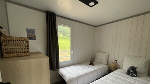 A bedroom with two beds, a wooden dresser, a wicker basket, a small figurine, and a poster on the wall. - Chalet Eguskitsua avec piscine (Hasparren)