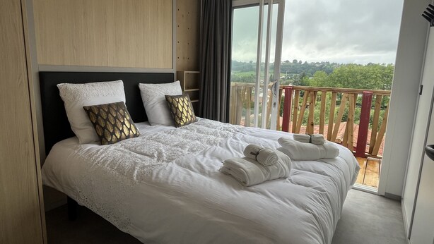 A hotel room with a large bed, a wooden headboard, and a balcony with a view of greenery. - Chalet Eguskitsua avec piscine (Hasparren)