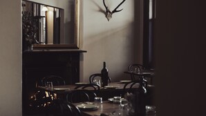 Un coin repas avec une table dressée pour quatre personnes, une bouteille de vin et un crâne de cerf accroché au mur.