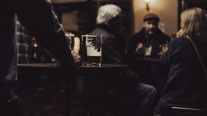 Un bar à la lumière tamisée, avec une table ronde, des verres de bière et des clients assis.