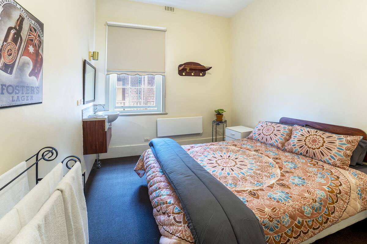 A bedroom with a bed, a window, a radiator, a towel rack, and a poster on the wall.